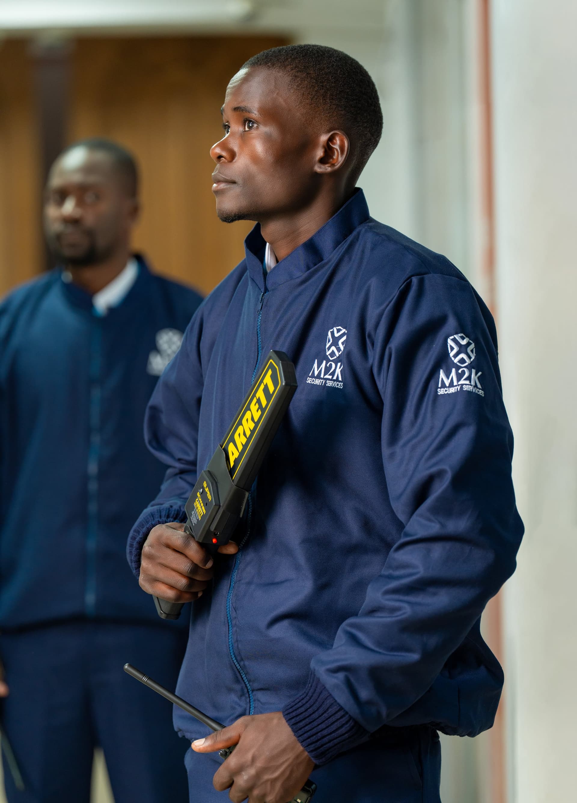 M2K guard performing a screening check with a metal detector